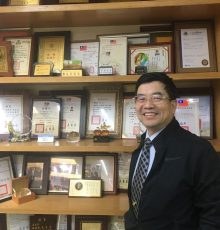 身着深色外套的男士站在摆满奖状与证书的陈列柜前